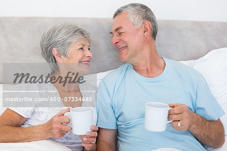 Senior couple with coffee cups while looking at each other in bed at home