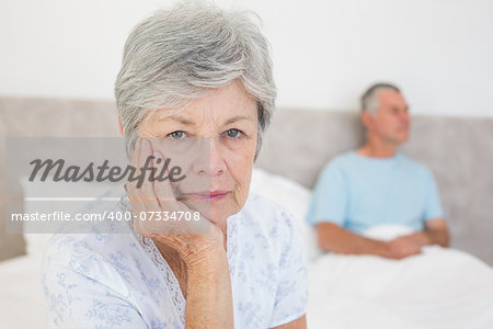 Portrait of disappointed senior woman with husband in background at home