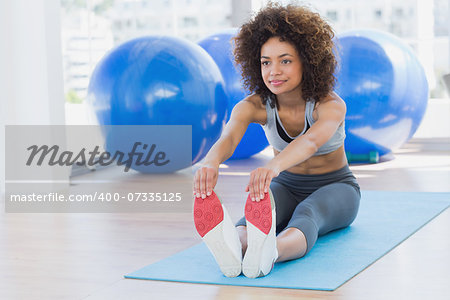 Full length of a sporty young woman stretching hands to legs in fitness studio