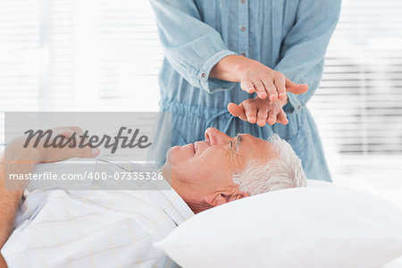 Massage therapist performing Reiki over forehead of senior man at health spa