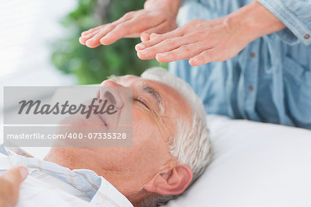 Massage therapist performing Reiki over senior man at health spa