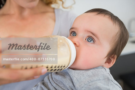 Mother feeding milk to baby boy from bottle at home