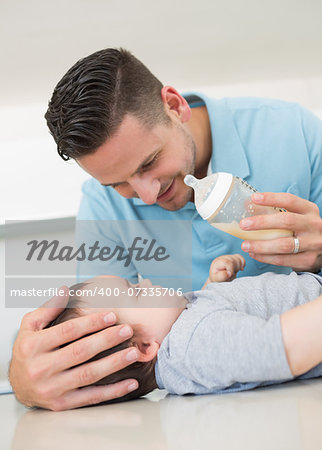Loving father feeding milk to baby boy at kitchen counter
