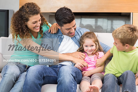 Cute family tickling little girl on the couch at home in living room