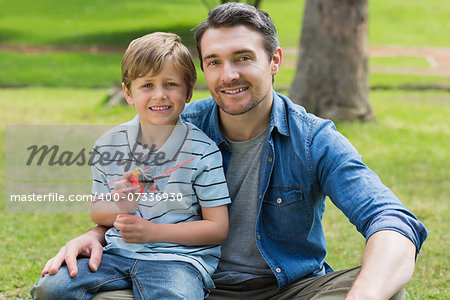 Portrait of a young boy with toy aeroplane sitting on father's lap at the park