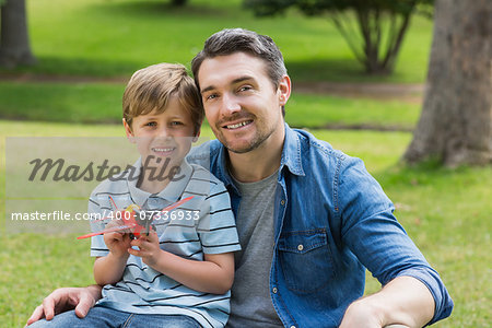 Portrait of a young boy with toy aeroplane sitting on father's lap at the park