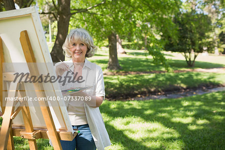 Portrait of a smiling mature woman painting on canvas in the park