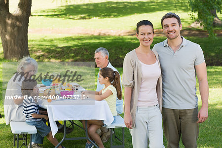 Portrait of a couple with family having lunch in background at the lawn