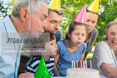 Cheerful extended family wearing party hats and blowing birthday cake in the park