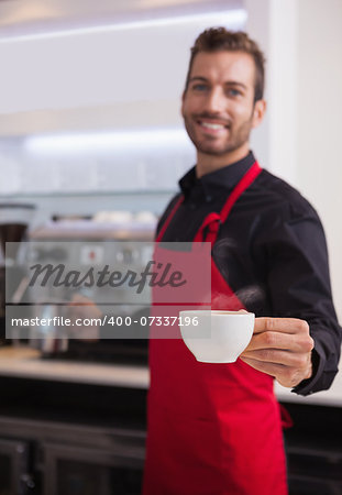 Smiling young barista holding jug and cup of coffee in a cafe
