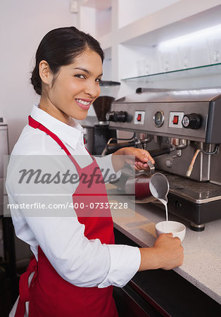 Pretty barista pouring milk into cup of coffee in a cafe