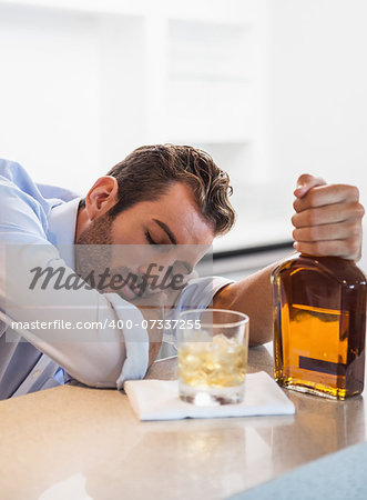 Drunk businessman clutching whiskey bottle asleep at the local bar