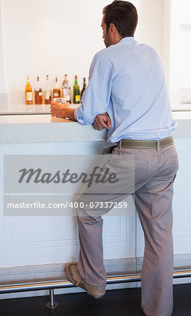 Businessman standing at the bar holding glass of whiskey at the local bar