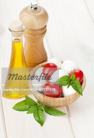 Mozzarella cheese with cherry tomatoes, basil and olive oil with pepper shaker on white wood table