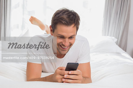 Happy casual young man text messaging in bed at home