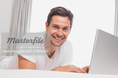 Portrait of a relaxed casual young man using laptop in bed at home