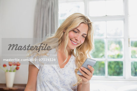 Happy casual young woman reading text message in bed at home