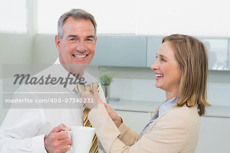 Side view of a woman adjusting businessman's tie in the kitchen at home