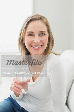 Portrait of a smiling relaxed woman with a glass of water in living room at home