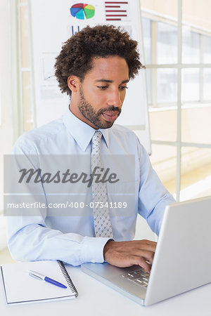 Concentrated young businessman using laptop at office desk