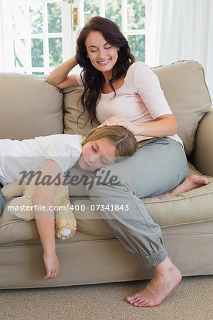 Loving mother looking at daughter sleeping on her lap in living room