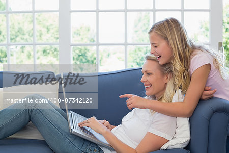 Happy girl pointing at laptop while mother using it on sofa at home