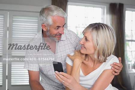 Happy mature couple looking at each other while reading text message at home