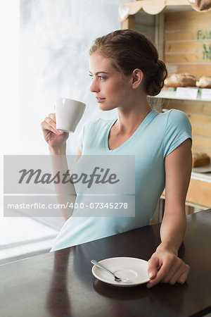 Thoughtful young woman drinking coffee at counter in the coffee shop