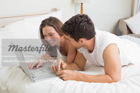 Smiling young couple using laptop in bed at home