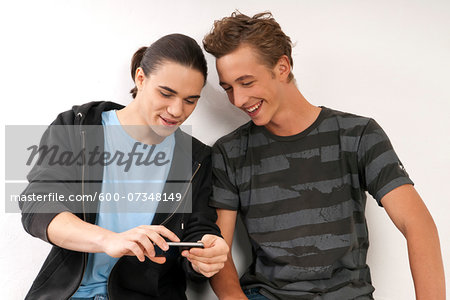 Two young men, friends looking at cell phone together, studio shot on white background