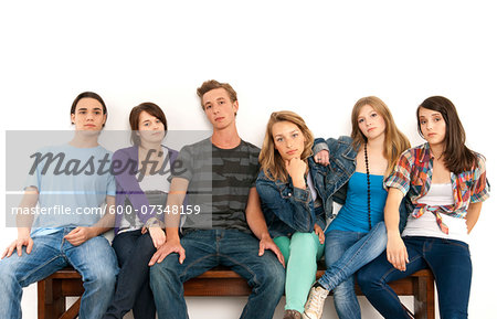 Portrait of six young people sitting together on a bench, studio shot on white background