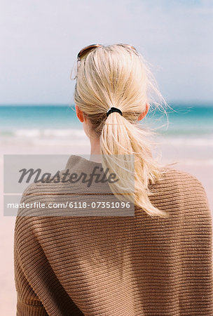 A blonde haired woman looking out to sea from the shore.