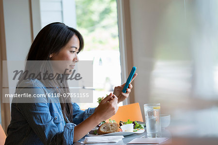 A woman eating a salad, and checking her phone.
