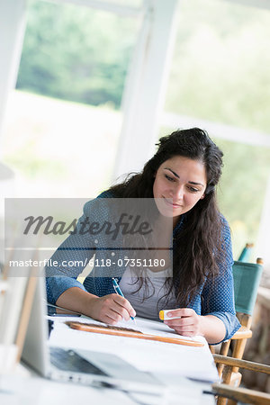 A woman working at a table, using a digital tablet.