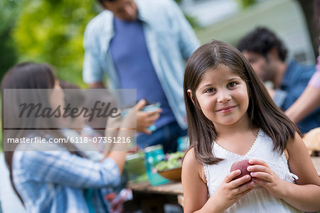 A summer party outdoors. Adults and children around a table.