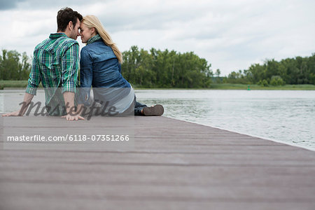 A man and woman seated on a jetty by a lake. A man and woman seated on a jetty by a lake.