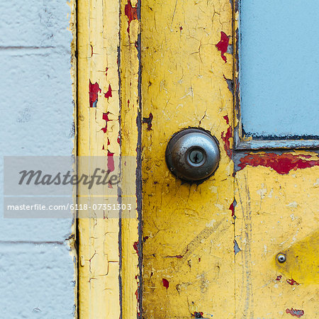 A doorway and the doorbell of a building. Flaked damaged paint.