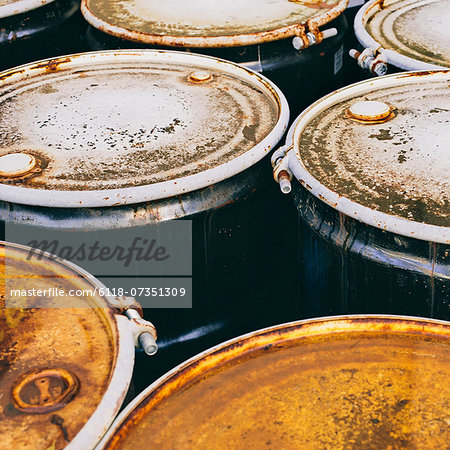 A group of rusted corroded barrels of chemical or petroleum products.