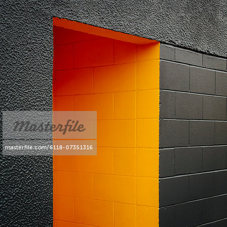 A doorway recess, painted orange in a grey block concrete wall.
