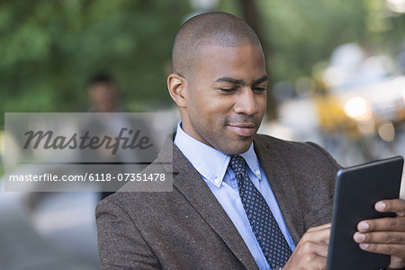 Business people in the city. Keeping in touch on the move. Two men in the park, one using a digital tablet, and one checking a smart phone.