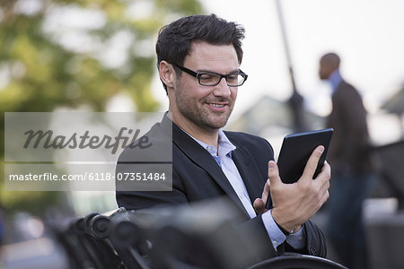 Business people in the city. Keeping in touch on the move. A man seated on a bench, using a digital tablet.