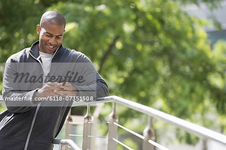 Business people in the city. Keeping in touch on the move. A man in a sweatshirt, leaning on a railing in the park, looking down at his smart phone.