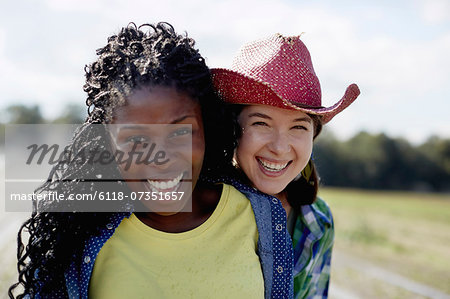 Two young women standing together with a sprinkler system working in the background.