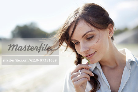 A young woman with windblown hair with a small green sprig of plant material in her hand.