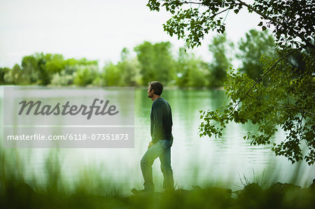 A man standing alone looking into the distance across the water, deep in thought.