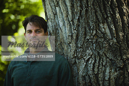 A man standing by a large tree with gnarled ridged bark.