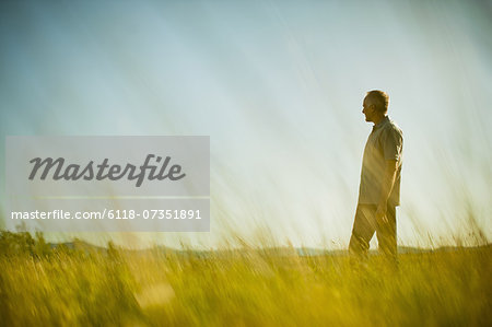 A man standing in grassland, looking into the distance.