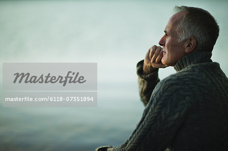 A mature man with grey hair, looking out over water, into the distance.