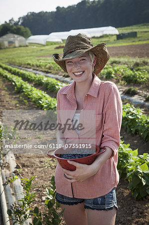 A girl in a pink shirt holding a large bowl of harvested blueberry fruits.