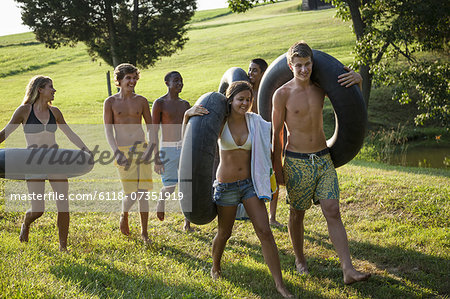 A group of young people, boys and girls, holding towels and swim floats, going for a swim.